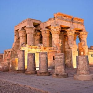 Temple of Kom Ombo in Egypt illuminated at dusk, showcasing ancient stone columns with detailed carvings.