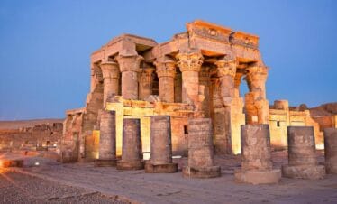 Temple of Kom Ombo in Egypt illuminated at dusk, showcasing ancient stone columns with detailed carvings.