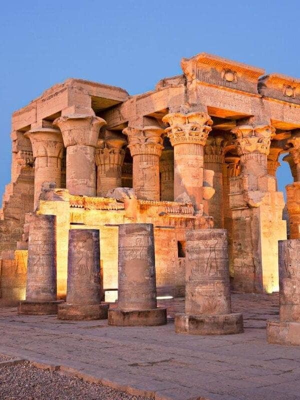 Temple of Kom Ombo in Egypt illuminated at dusk, showcasing ancient stone columns with detailed carvings.