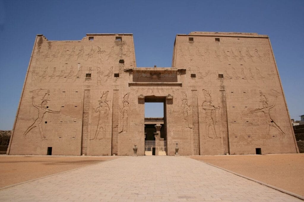 Temple of Edfu in Egypt with massive sandstone walls carved with ancient hieroglyphs and pharaonic reliefs.