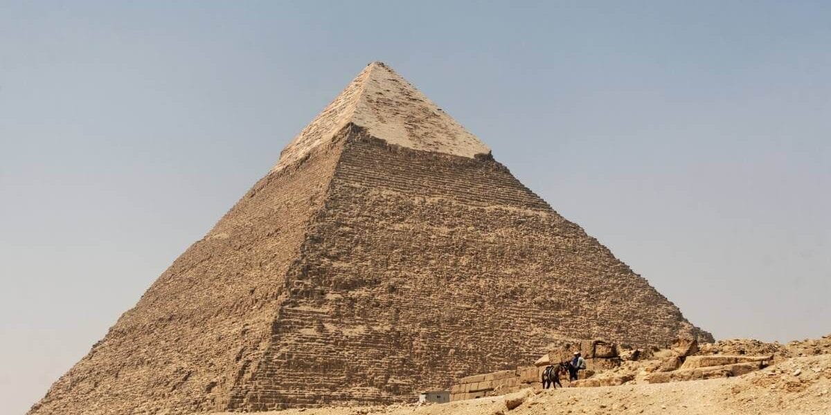 Pyramid of Chephren in Giza, Egypt, with limestone casing at the top and desert landscape below.