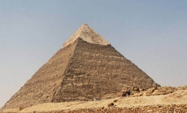 Pyramid of Chephren in Giza, Egypt, with limestone casing at the top and desert landscape below.