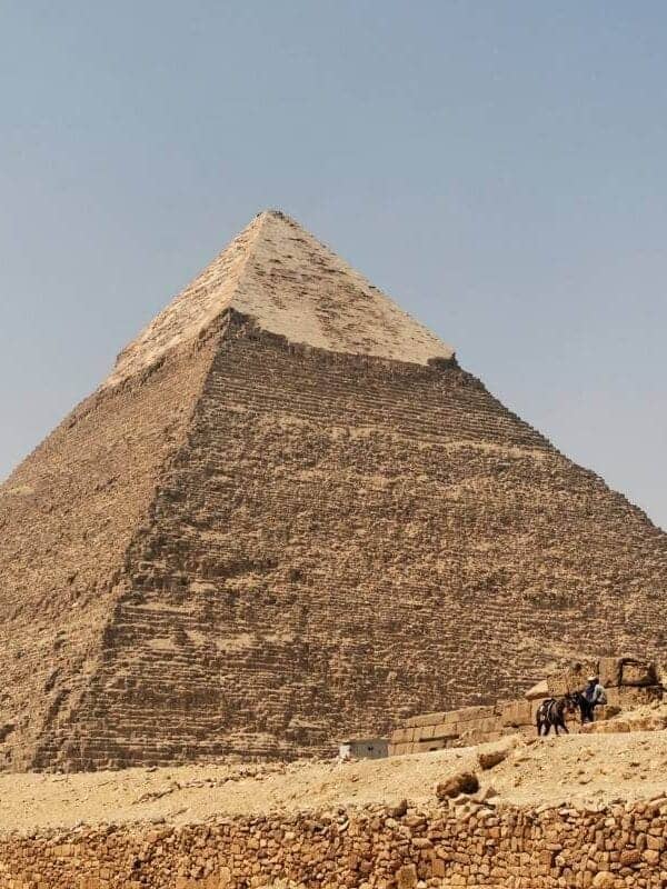 Pyramid of Chephren in Giza, Egypt, with limestone casing at the top and desert landscape below.