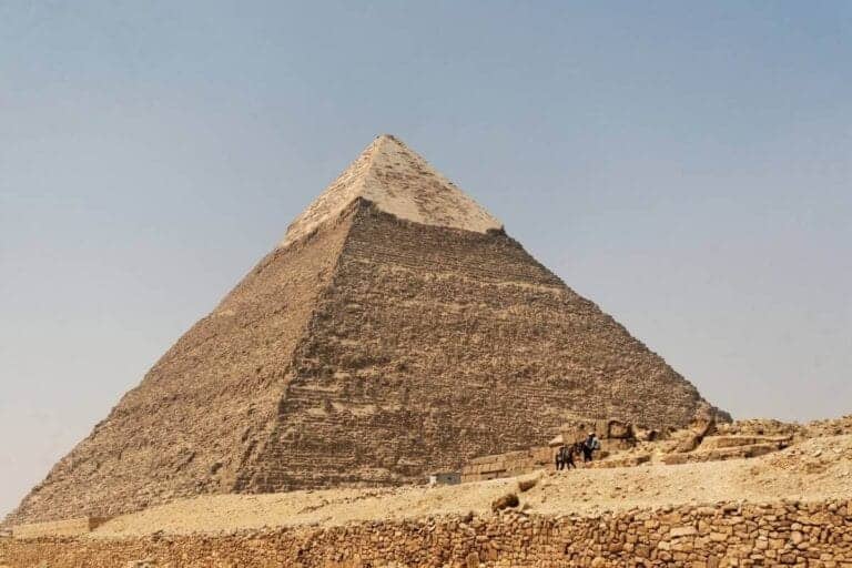 Pyramid of Chephren in Giza, Egypt, with limestone casing at the top and desert landscape below.