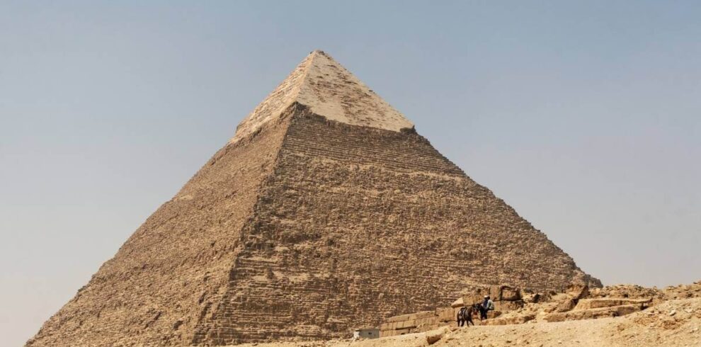 Pyramid of Chephren in Giza, Egypt, with limestone casing at the top and desert landscape below.
