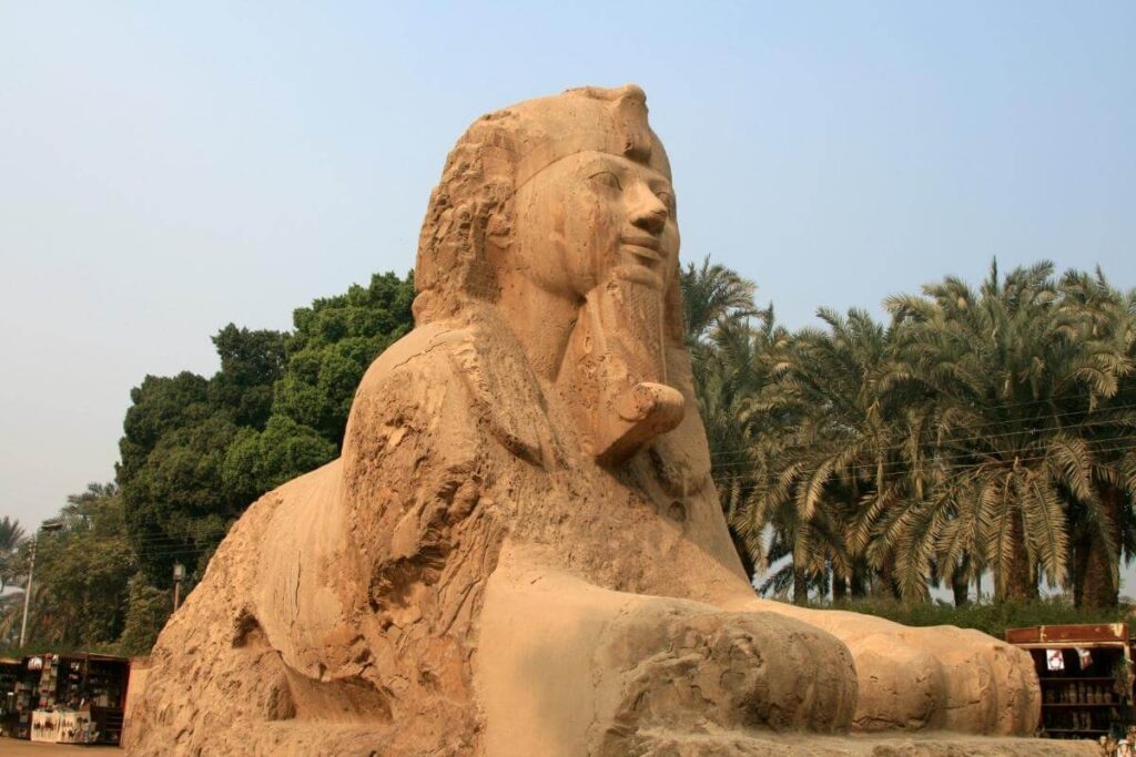 Alabaster Sphinx of Memphis in Egypt, carved from stone with a pharaoh’s face and lion’s body surrounded by palm trees.