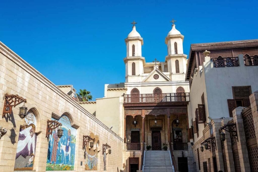 The Hanging Church in Cairo with twin bell towers, arched mosaics, and stone walls under a clear blue sky.