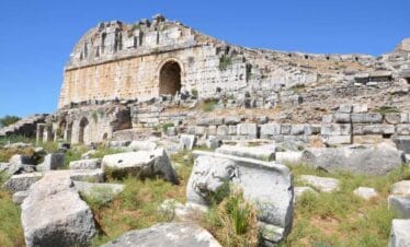 Ruins of Miletos Ancient Theatre in Turkey with stone seating, arched entrance, and carved lion relief under a clear blue sky.