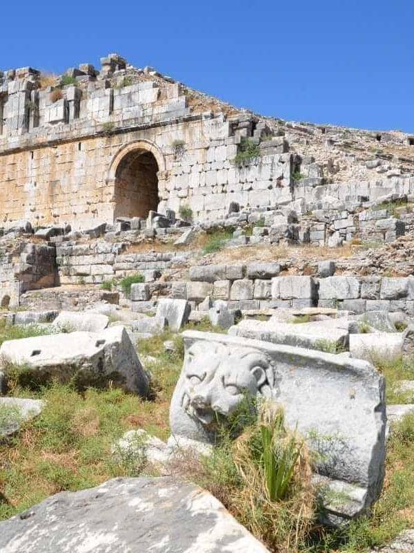 Ruins of Miletos Ancient Theatre in Turkey with stone seating, arched entrance, and carved lion relief under a clear blue sky.