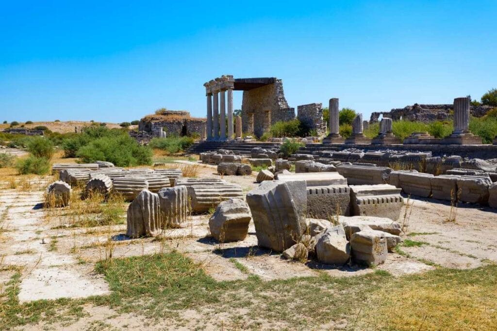 Ruins of Miletus Archaeological Site near Didim, Turkey, with scattered stone columns and ancient structures under a clear blue sky.