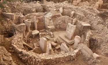 Ancient stone circle ruins of Göbekli Tepe with tall T-shaped pillars and stone walls in southeastern Turkey.