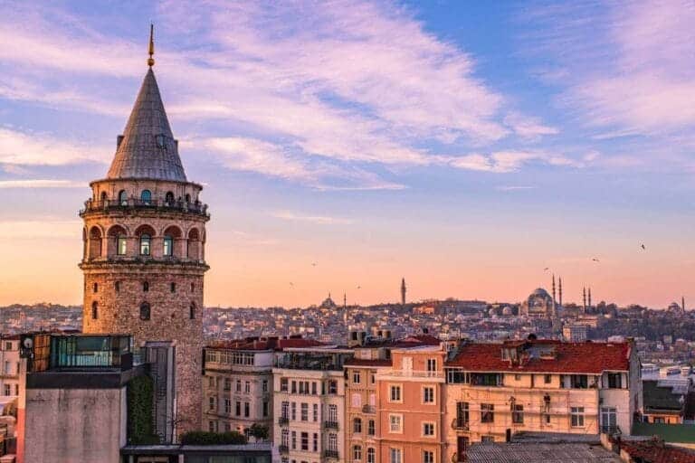 Galata Tower in Istanbul at sunset with historic city skyline and mosques under a colorful sky.