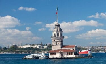 Maiden’s Tower on the Bosphorus with Turkish flag, boats nearby, and Istanbul skyline in the background.