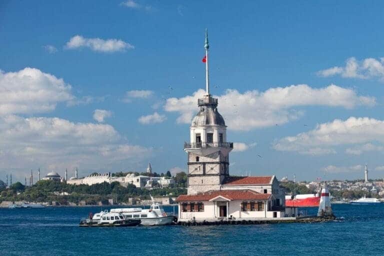 Maiden’s Tower on the Bosphorus with Turkish flag, boats nearby, and Istanbul skyline in the background.