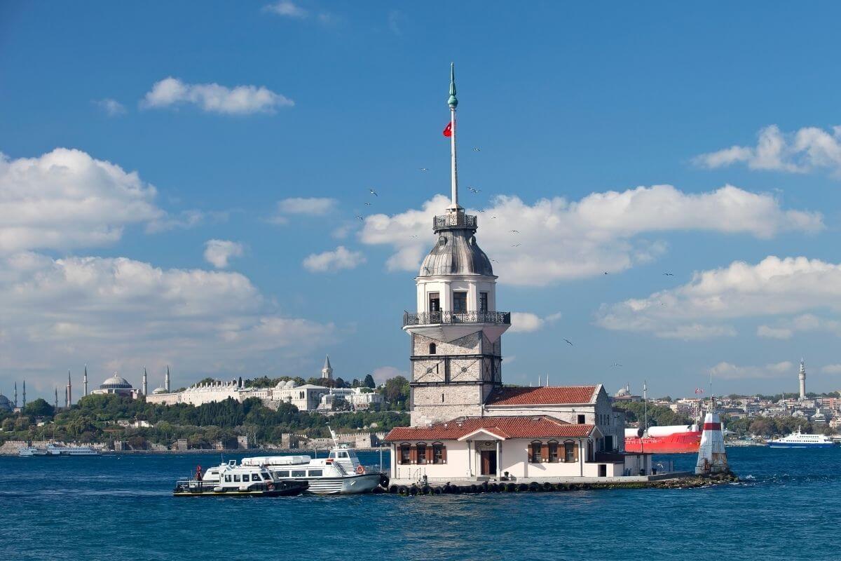 Maiden’s Tower on the Bosphorus with Turkish flag, boats nearby, and Istanbul skyline in the background.