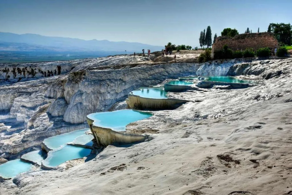 Natural travertine terraces with turquoise thermal pools at Pamukkale under a clear blue sky.