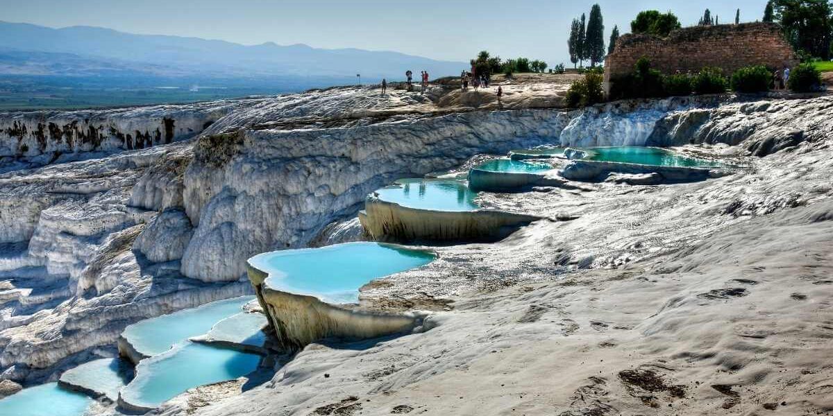 Natural travertine terraces with turquoise thermal pools at Pamukkale under a clear blue sky.
