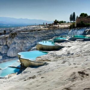 Natural travertine terraces with turquoise thermal pools at Pamukkale under a clear blue sky.
