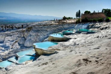 Natural travertine terraces with turquoise thermal pools at Pamukkale under a clear blue sky.