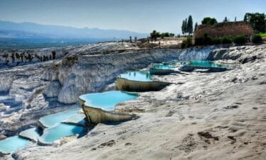 Natural travertine terraces with turquoise thermal pools at Pamukkale under a clear blue sky.