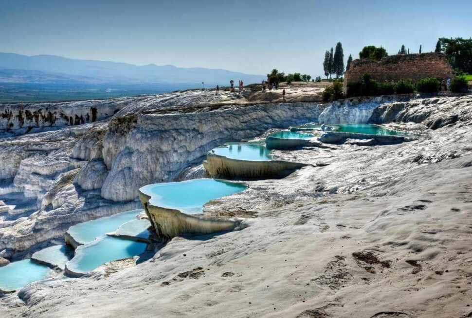 Natural travertine terraces with turquoise thermal pools at Pamukkale under a clear blue sky.