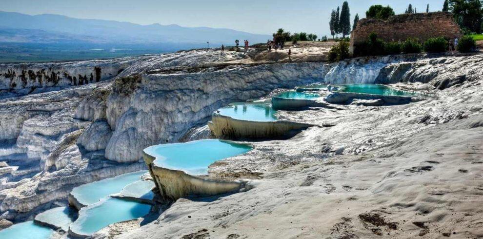 Natural travertine terraces with turquoise thermal pools at Pamukkale under a clear blue sky.
