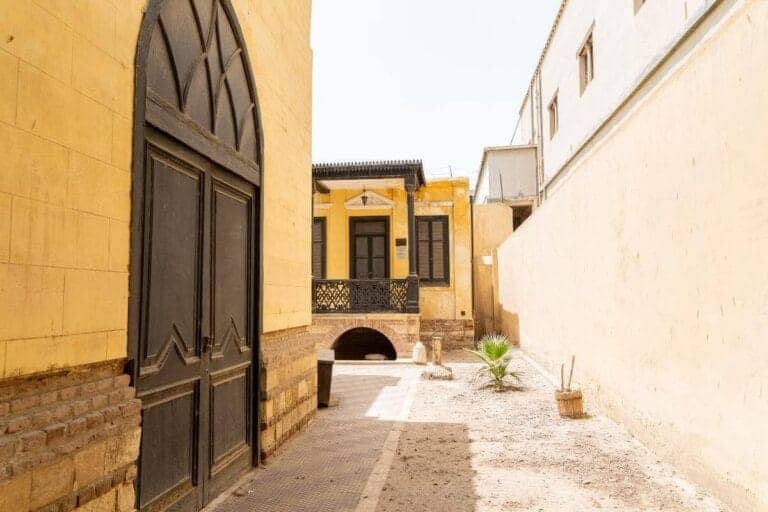 The Ben Ezra Synagogue in Cairo with yellow stone walls, arched doorway, and black wooden windows.