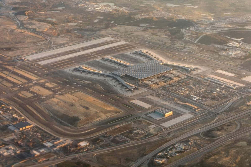Aerial view of a modern international airport terminal with wide runways and surrounding transport roads.