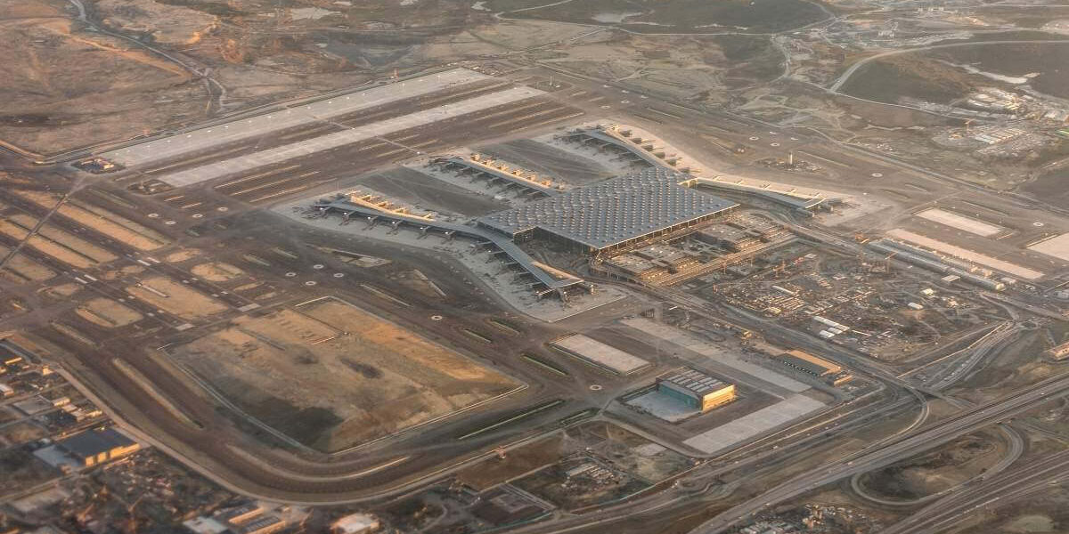 Aerial view of a modern international airport terminal with wide runways and surrounding transport roads.