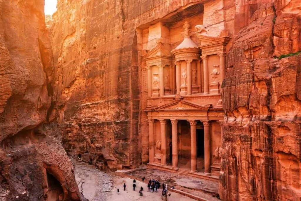 Petra Treasury in Jordan framed by sandstone cliffs, with intricate Nabatean carvings and visitors at the entrance.
