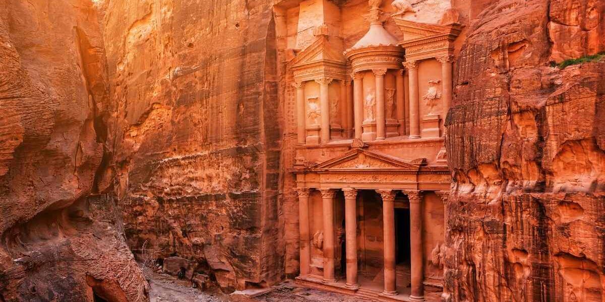 Petra Treasury in Jordan framed by sandstone cliffs, with intricate Nabatean carvings and visitors at the entrance.