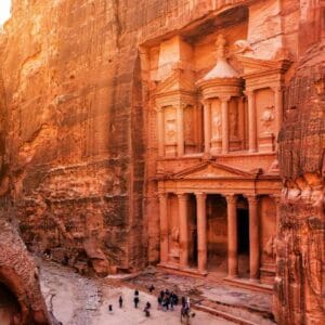 Petra Treasury in Jordan framed by sandstone cliffs, with intricate Nabatean carvings and visitors at the entrance.