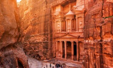 Petra Treasury in Jordan framed by sandstone cliffs, with intricate Nabatean carvings and visitors at the entrance.