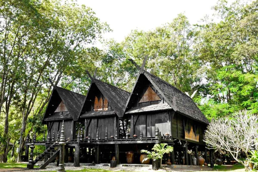 Black House Museum in Chiang Rai featuring traditional dark wooden structures surrounded by lush green trees.