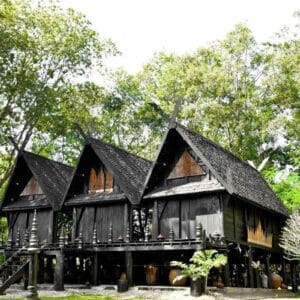 Black House Museum in Chiang Rai featuring traditional dark wooden structures surrounded by lush green trees.