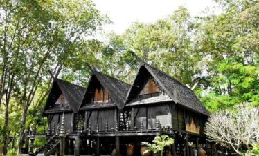 Black House Museum in Chiang Rai featuring traditional dark wooden structures surrounded by lush green trees.