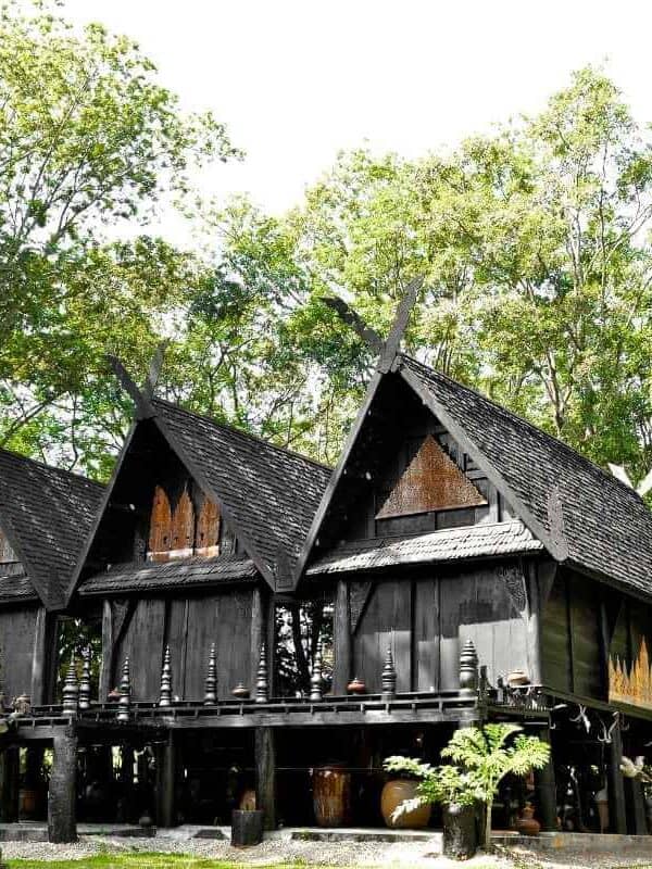Black House Museum in Chiang Rai featuring traditional dark wooden structures surrounded by lush green trees.