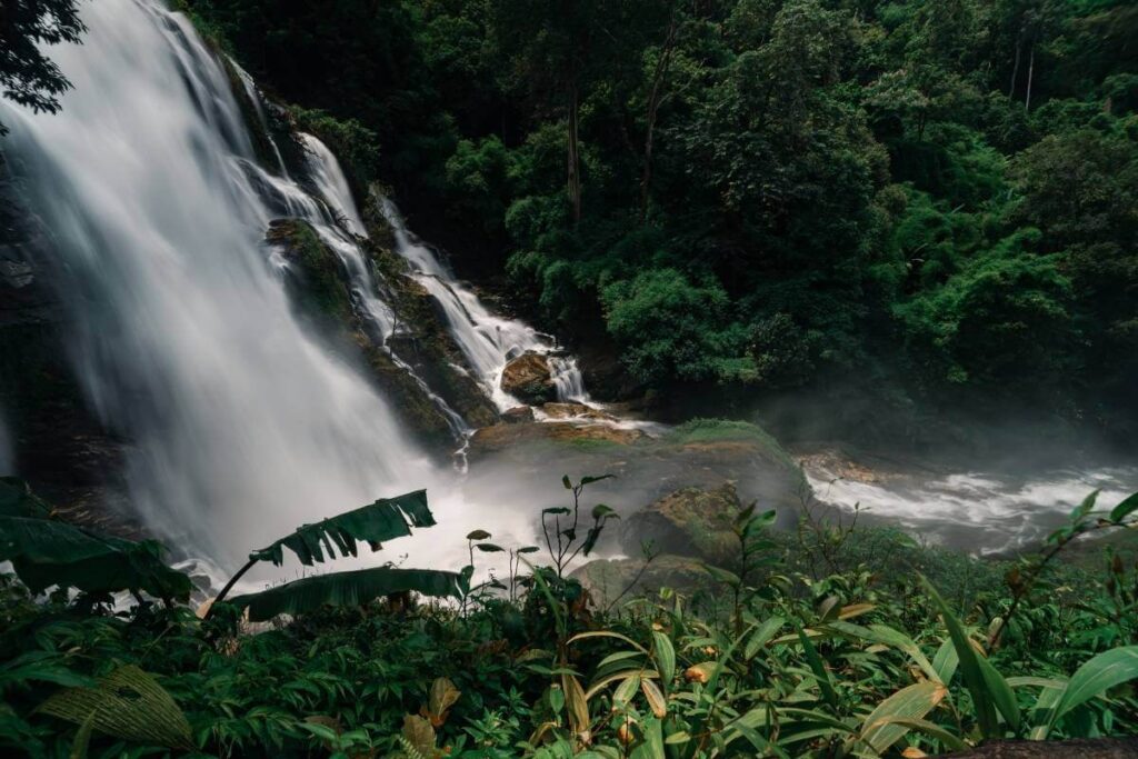 Wachiratharn Waterfall cascading through rocks in a lush jungle near Chiang Mai, Thailand, surrounded by vibrant greenery.