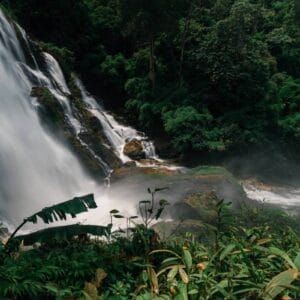 Wachiratharn Waterfall cascading through rocks in a lush jungle near Chiang Mai, Thailand, surrounded by vibrant greenery.
