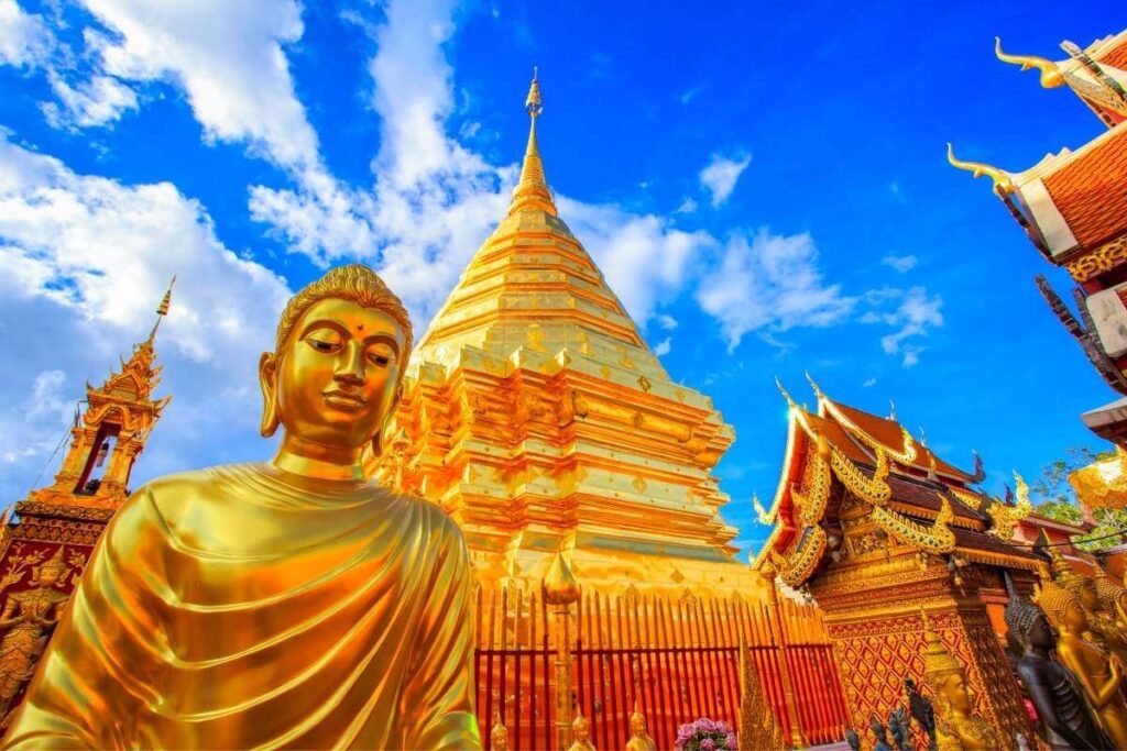 Golden Buddha statue and gleaming pagoda at Wat Phra That Doi Suthep temple in Chiang Mai, Thailand under bright blue sky.