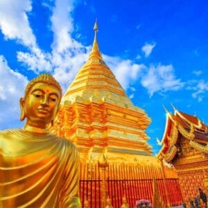 Golden Buddha statue and gleaming pagoda at Wat Phra That Doi Suthep temple in Chiang Mai, Thailand under bright blue sky.
