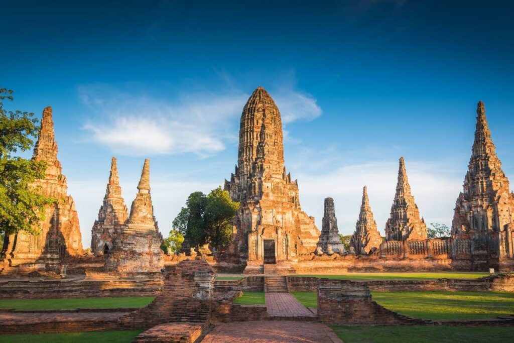 Ancient ruins of Wat Chaiwatthanaram temple in Ayutthaya, Thailand, with tall prangs and red brick structures under blue sky.