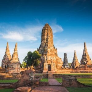 Ancient ruins of Wat Chaiwatthanaram temple in Ayutthaya, Thailand, with tall prangs and red brick structures under blue sky.