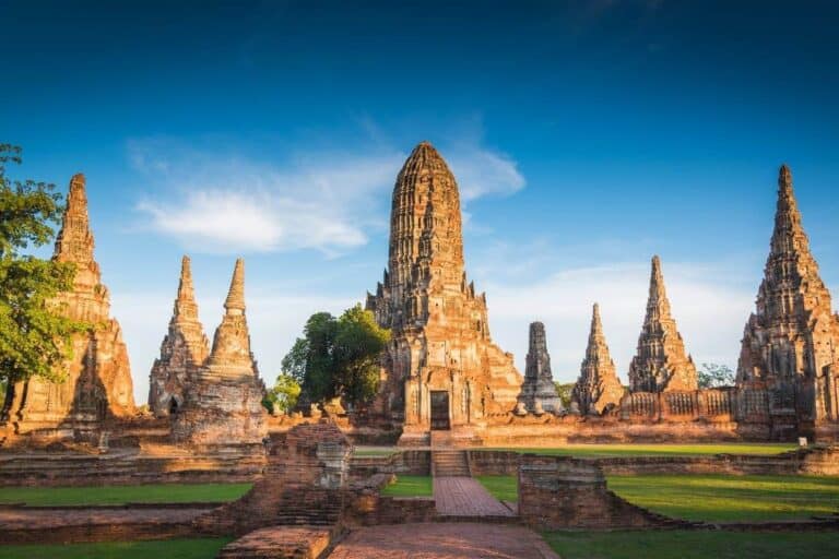 Ancient ruins of Wat Chaiwatthanaram temple in Ayutthaya, Thailand, with tall prangs and red brick structures under blue sky.