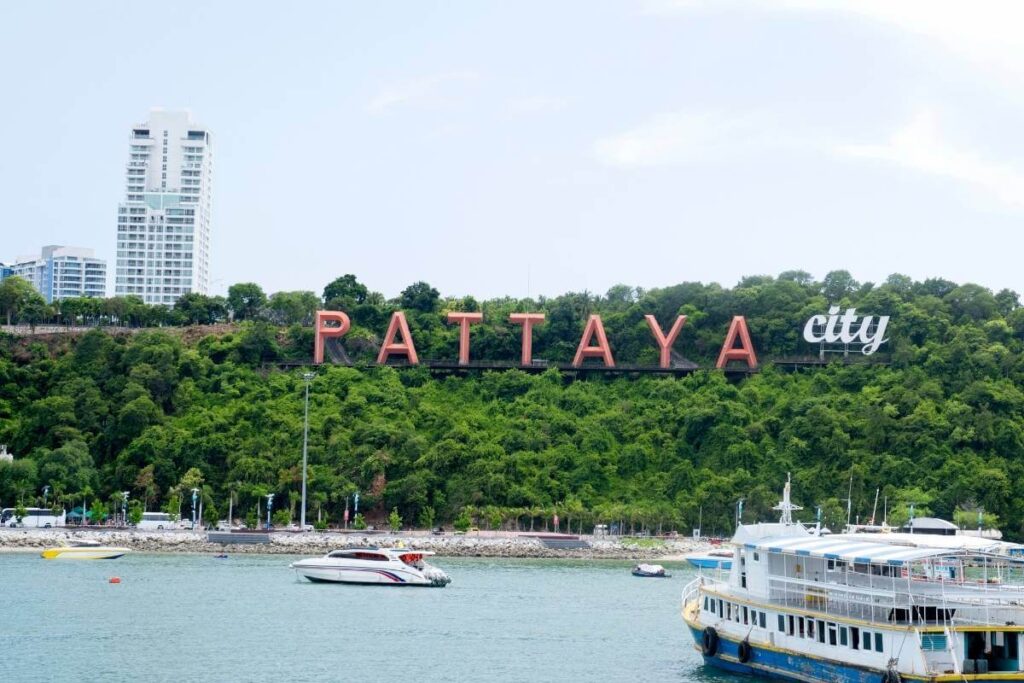 Pattaya City sign on a green hillside overlooking the bay with boats and modern buildings in the background, Thailand.
