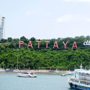 Pattaya City sign on a green hillside overlooking the bay with boats and modern buildings in the background, Thailand.