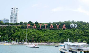 Pattaya City sign on a green hillside overlooking the bay with boats and modern buildings in the background, Thailand.