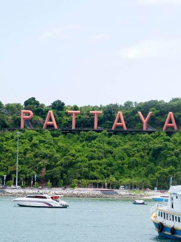 Pattaya City sign on a green hillside overlooking the bay with boats and modern buildings in the background, Thailand.