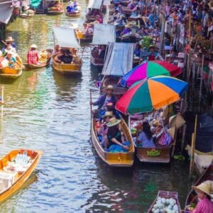 Colorful floating market in Thailand with vendors selling goods from wooden boats under umbrellas on a busy canal.