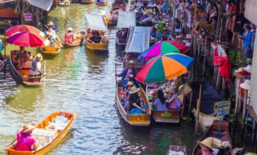 Colorful floating market in Thailand with vendors selling goods from wooden boats under umbrellas on a busy canal.